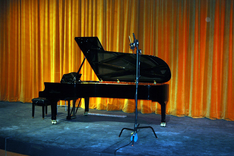 A prototype SF-24V and a stock SF-24 on stands pulled back from a piano at a live concert